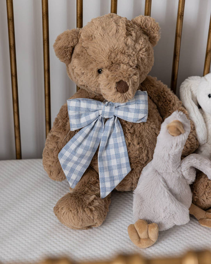 Baby blue gingham fabric bow displayed on a teddy bear in a storybook nursery setting.