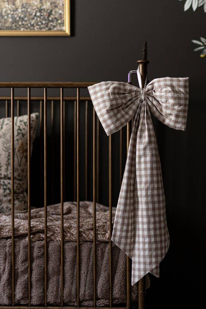 Large beige gingham crib bow displayed on a nursery crib with timeless cottage style.