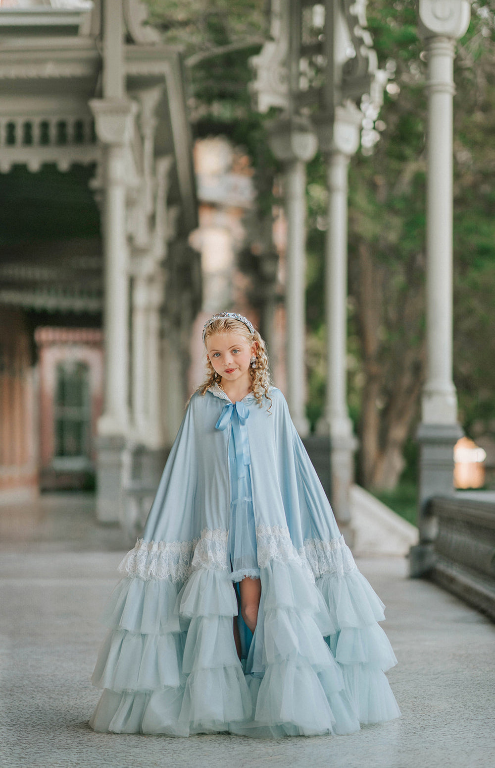 Full-length view of The Cendrillon pale blue princess cape with satin ribbon tie, white lace trim and tiered tulle ruffles