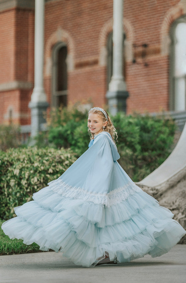 Girl twirling in The Cendrillon pale blue satin cape, showing the movement and volume of its cascading tulle ruffl