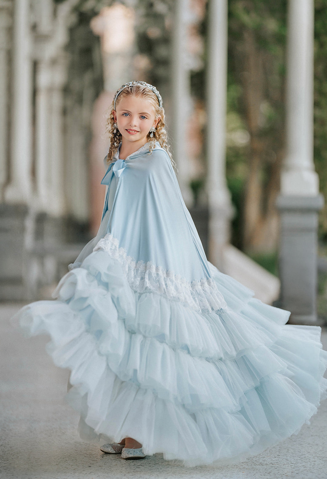 Girl wearing a Cinderella-inspired pale blue satin princess cape with lace-trimmed hood and layered tulle ruffles