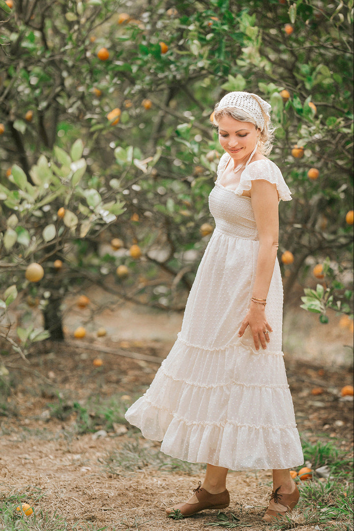 Side profile of Citrus Cream Swiss dot maxi dress with flutter sleeves and flowing tiered skirt