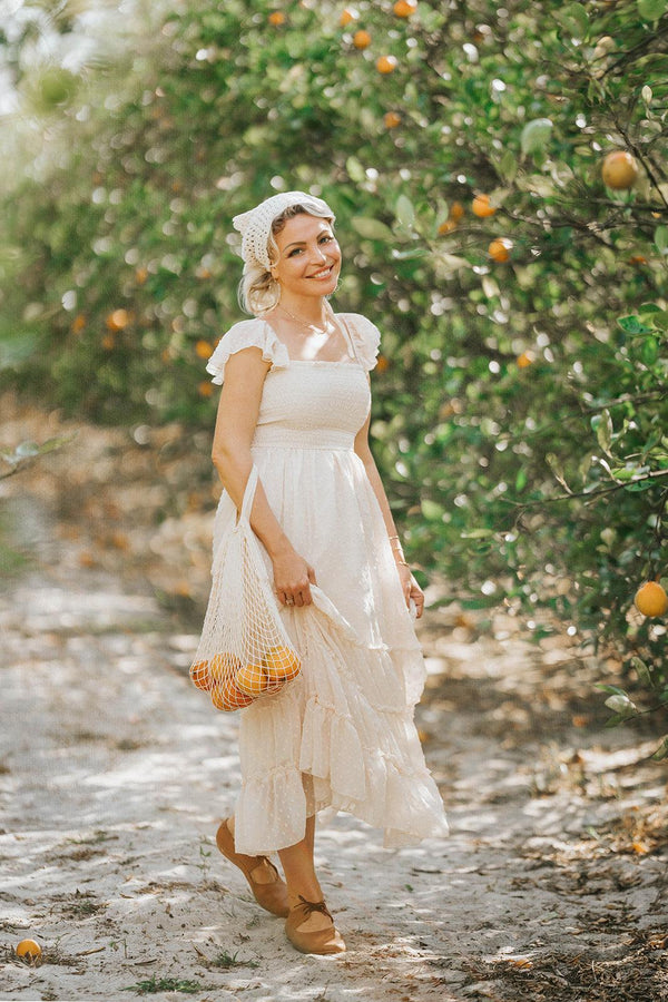 Woman wearing Citrus Cream Swiss dot maxi dress in an orange grove from the Orchard Collection