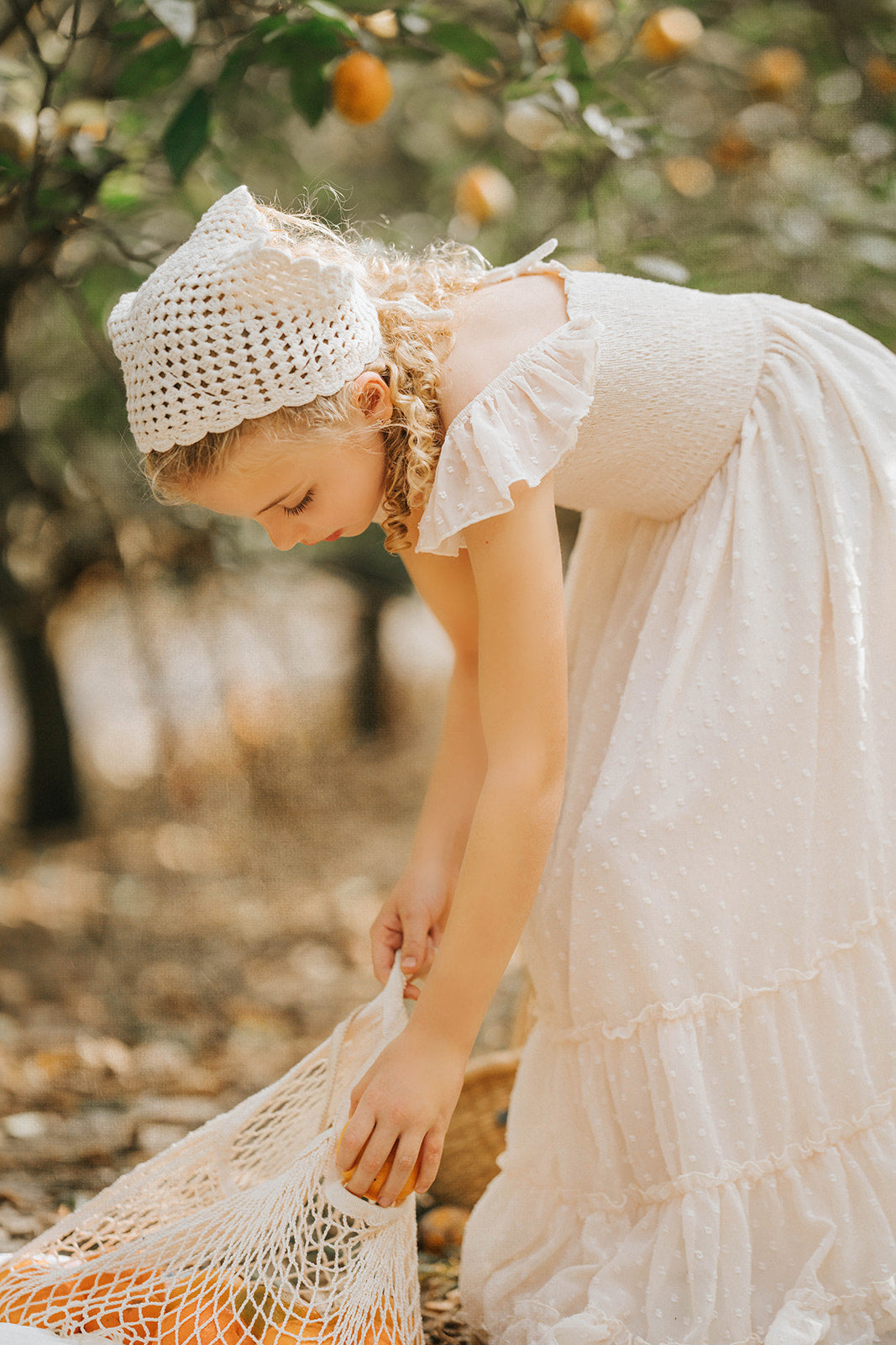 Close-up lifestyle image of a child gathering fruit while wearing the Citrus Cream Orchard Dress in an orchard setting