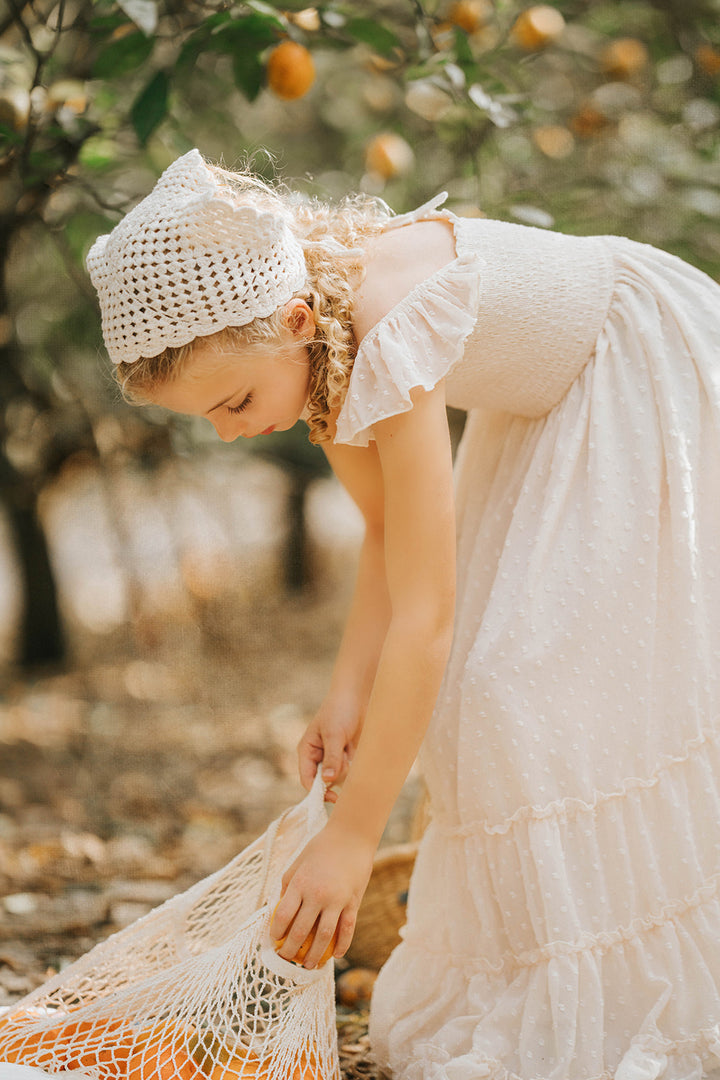 Close-up lifestyle image of a child gathering fruit while wearing the Citrus Cream Orchard Dress in an orchard setting