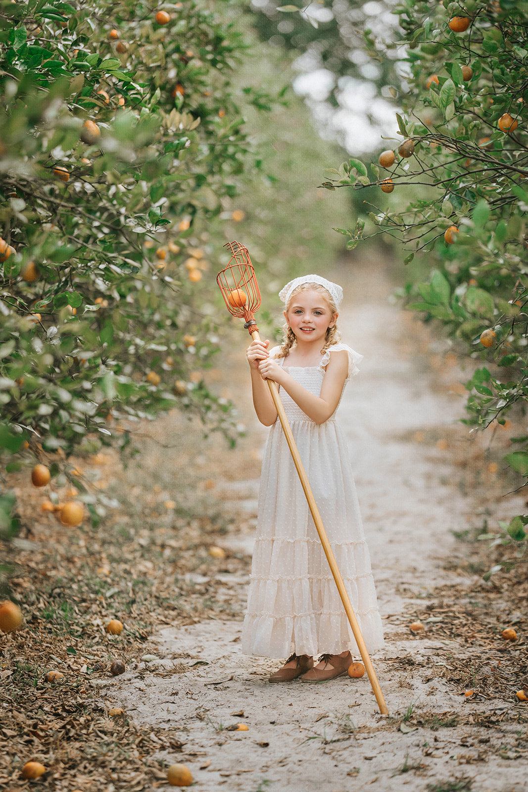 Girl in the Citrus Cream Orchard Dress walking along an orchard path surrounded by trees and golden afternoon light