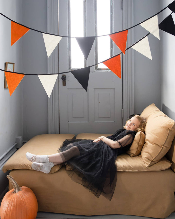 Little girl dressed for Halloween with vintage black orange and cream felt pennant banner displayed in the background