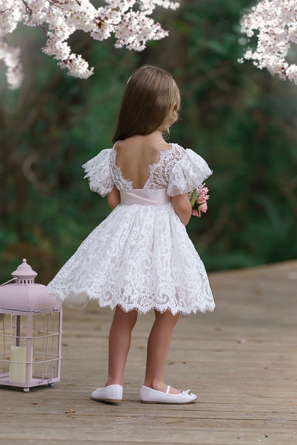 Back view of soft white lace flower girl dress with ruffle sleeves and tied satin bow sash, classic bridal party dress