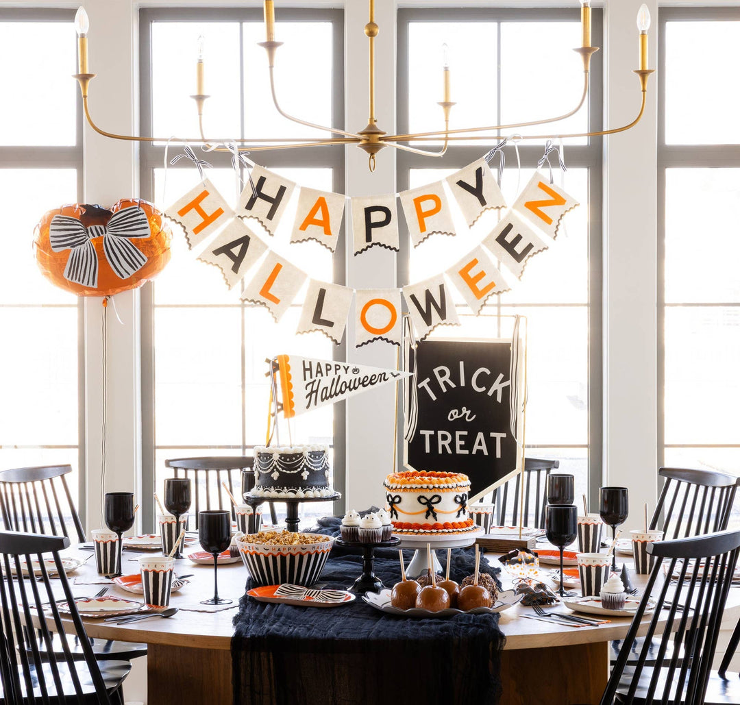 Felt Happy Halloween banner styled above a Halloween party table with pumpkins, treats and festive black and orange decorations.