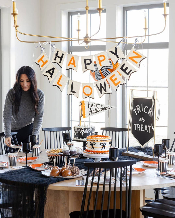 Felt Happy Halloween banner displayed over an elegant Halloween party table with pumpkins, black accents and orange seasonal decorations.