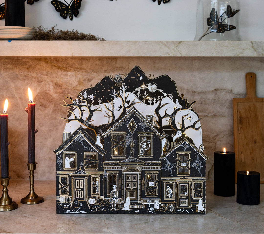 Three-dimensional haunted paper mansion with layered woodland backdrop and warm illuminated windows.