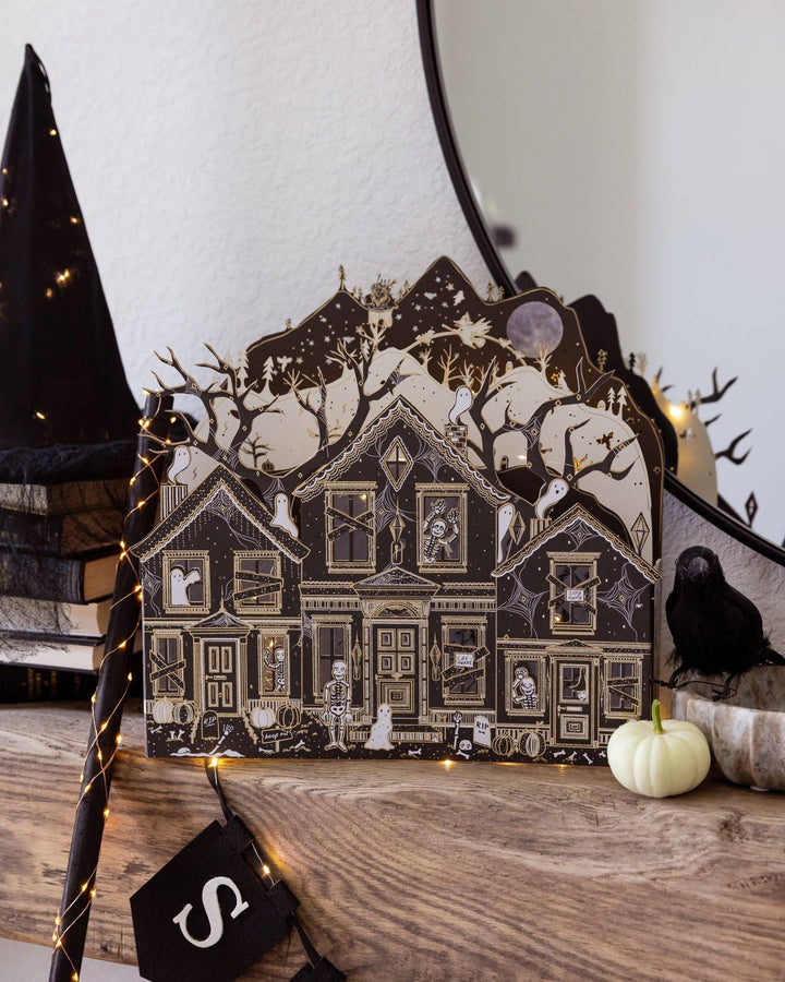 Illuminated haunted paper house with intricate black, ivory, and gold details displayed on a mantel for Halloween.