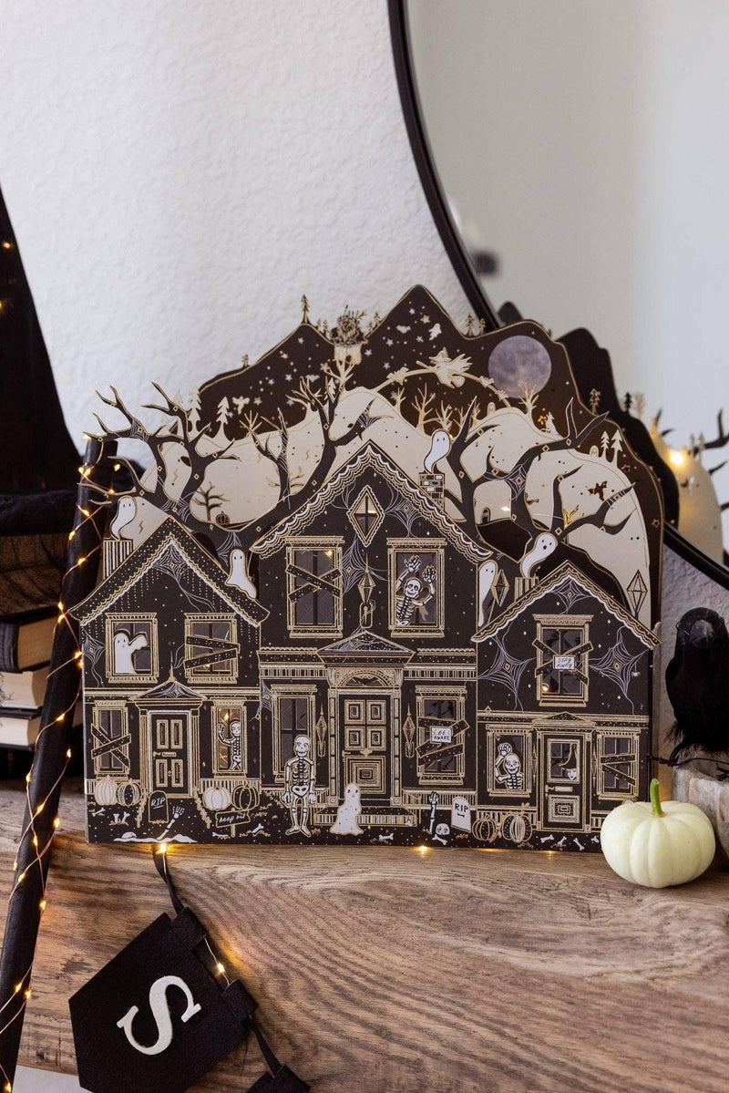 Illuminated haunted paper house with intricate black, ivory, and gold details displayed on a mantel for Halloween.
