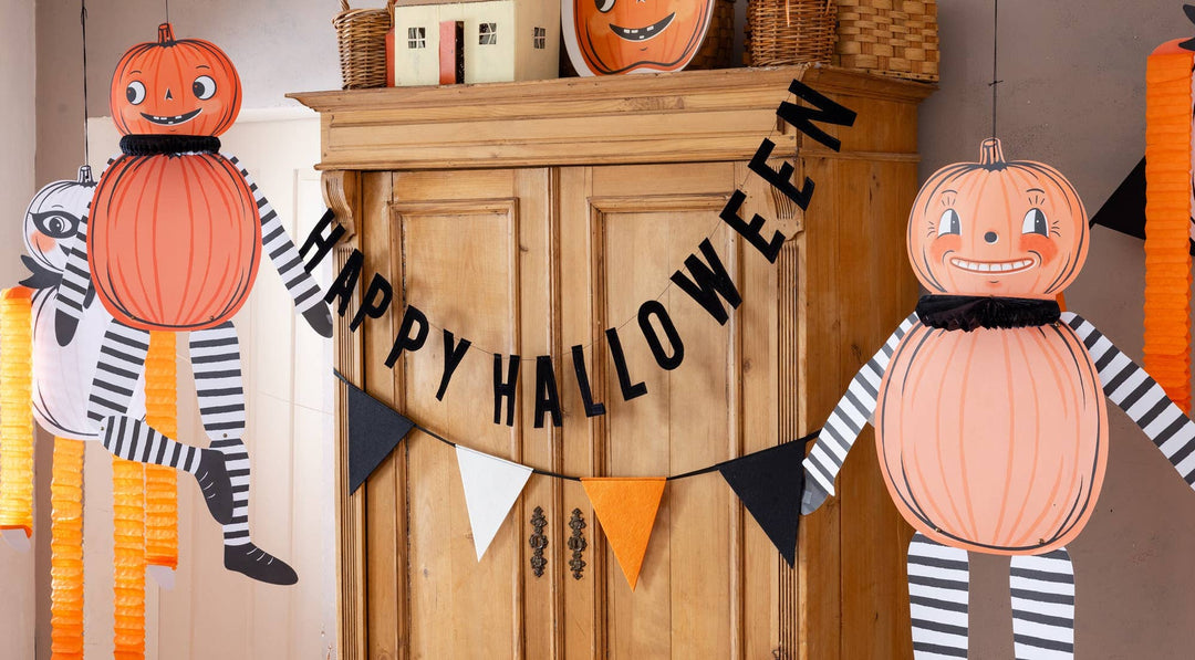Vintage Halloween felt pennant banner displayed above a festive table setting with pumpkins, treats and seasonal decorations