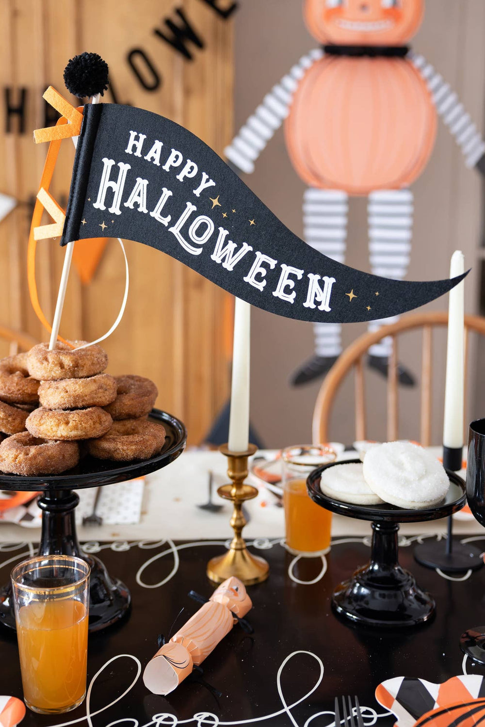 Happy Halloween felt pennant displayed over a Halloween party table with cider donuts, candles and orange black and white decorations
