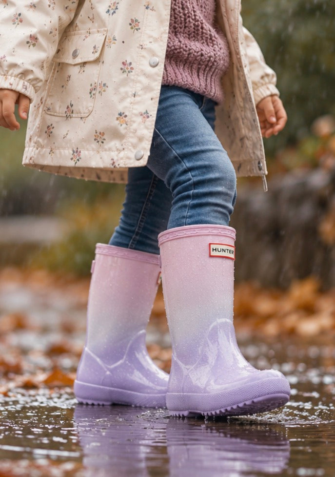 Child wearing Hunter  Boots Kids First Starcloud pink white and purple ombre waterproof rain boots while splashing in a puddle