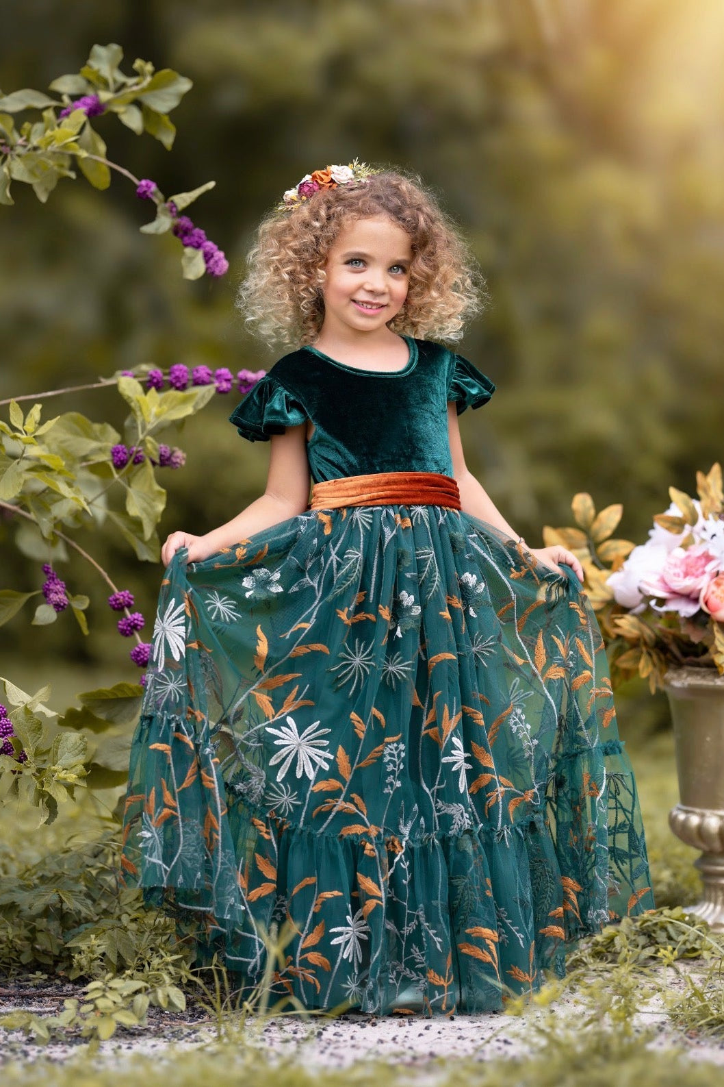 Girl wearing Virelle velvet flower girl dress in forest green with full-length embroidered tulle skirt outdoors