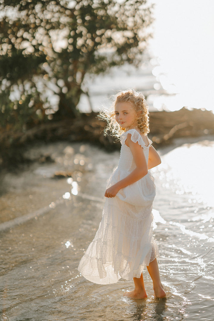 Side profile of a girl wearing the Orange Blossom Orchard Collection dress in soft white Swiss dot fabric.