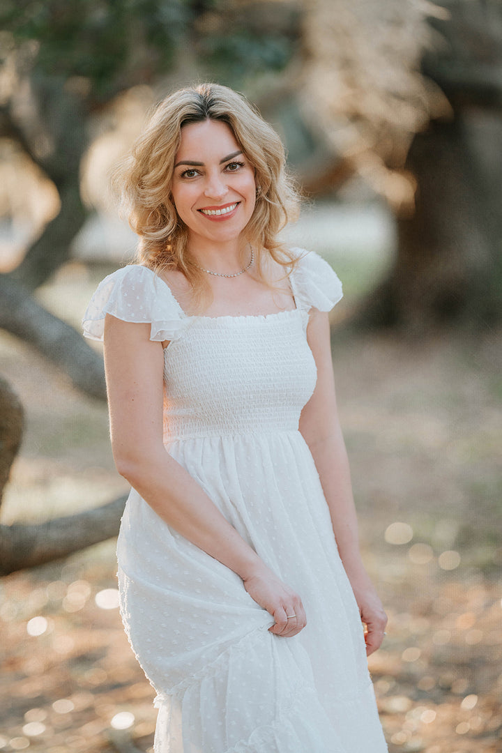 Close portrait of woman wearing the Orange Blossom Swiss dot maxi dress beneath moss-covered oak trees.