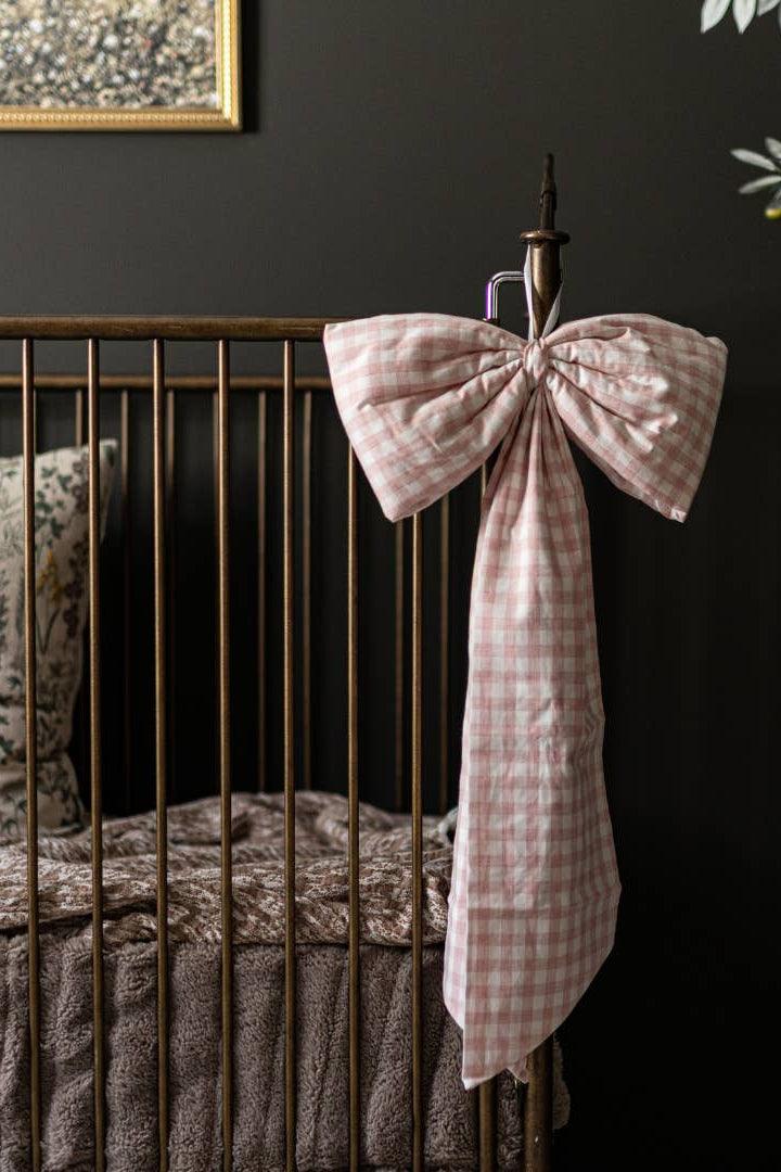 Large pink gingham crib bow styled on a nursery crib for timeless heirloom decor.