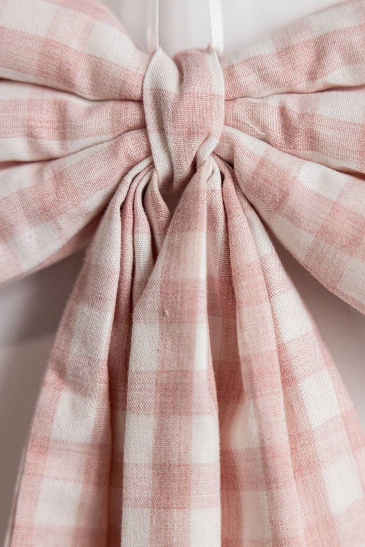 Close-up of handcrafted pink gingham fabric bow with flowing tails and cotton fabric.