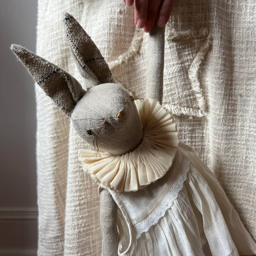 Handcrafted linen rabbit ragdoll wearing a cotton dress and ruffle collar in a storybook-inspired setting