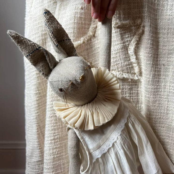 Handcrafted linen rabbit ragdoll wearing a cotton dress and ruffle collar in a storybook-inspired setting