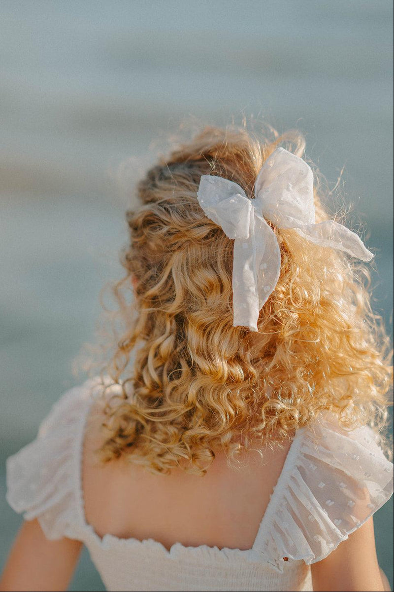 Swiss dot hair bow with long tails styled in curly hair from the Orchard Collection