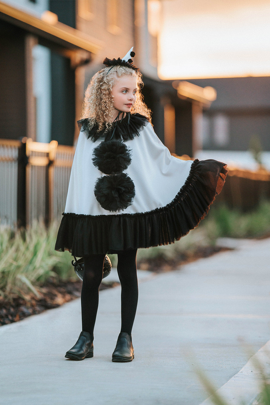 Model wearing the white satin Pirouette clown cape with black tulle ruffles, pom-poms and matching pointed clown hat.