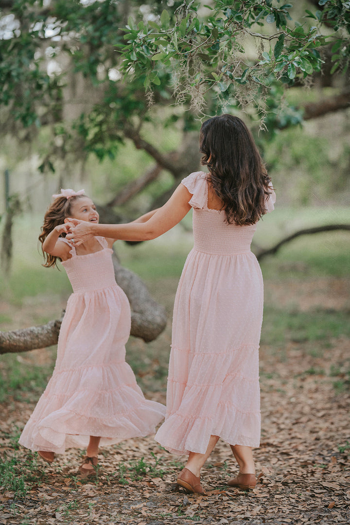 Mother and daughter twirling in matching Wild Strawberry Orchard Collection dresses beneath oak trees.