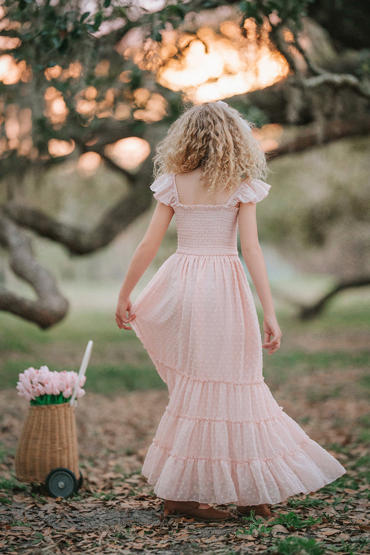 Girl wearing Wild Strawberry Swiss dot dress standing beside flower basket in an orchard