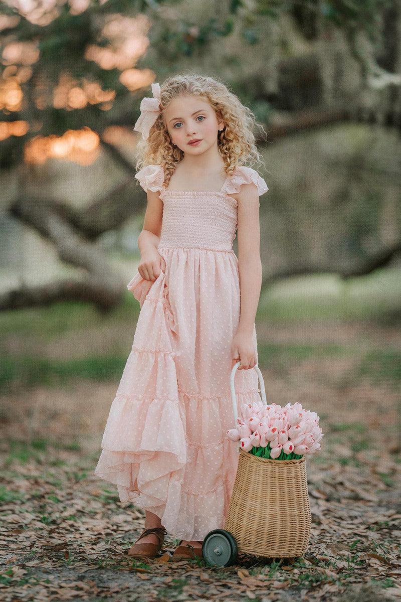 Girl wearing Wild Strawberry Swiss dot dress carrying a basket of pink flowers in an orchard setting