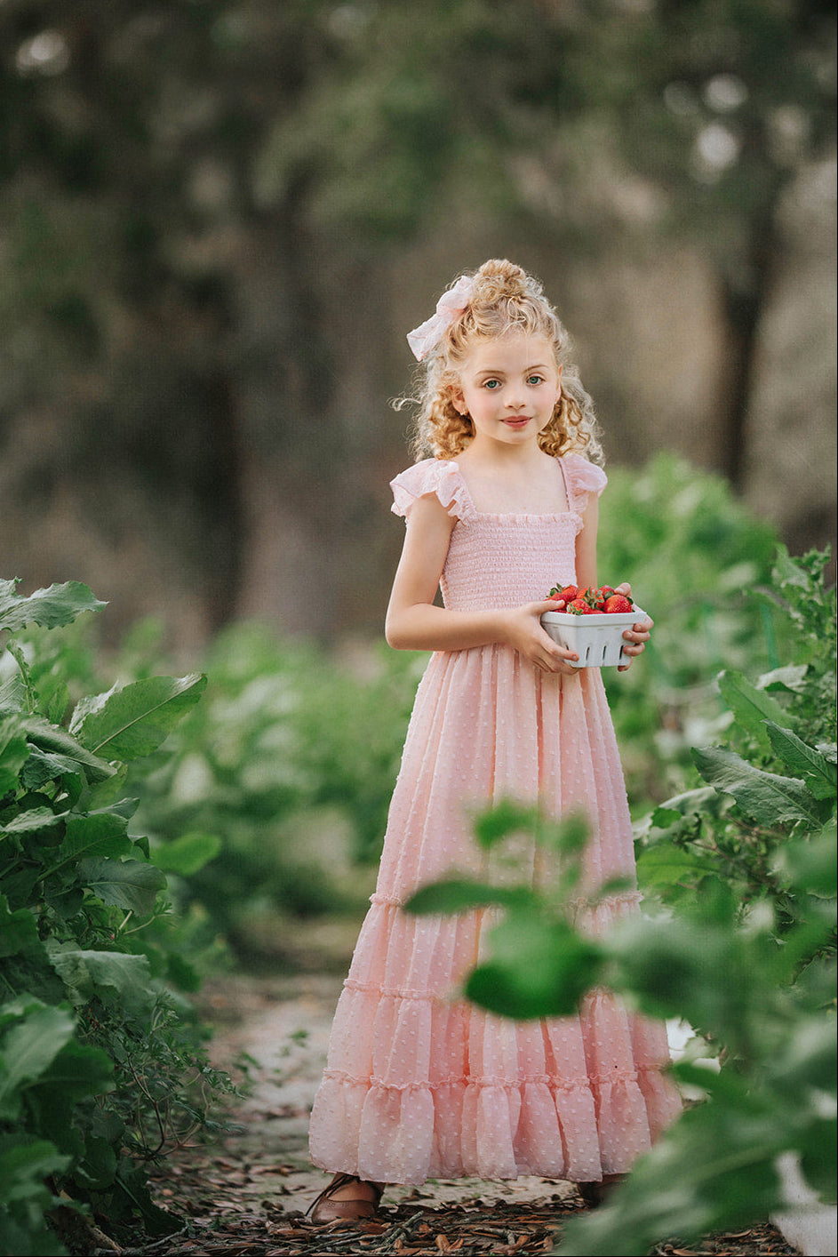 Girl in Wild Strawberry Swiss dot maxi dress holding fresh strawberries in a garden