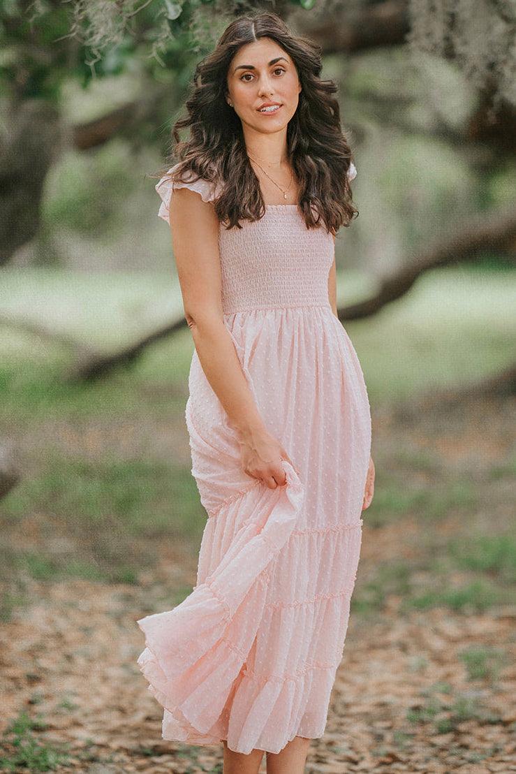 Woman walking through an orchard in the Wild Strawberry pink Swiss dot maxi dress with flutter sleeves.